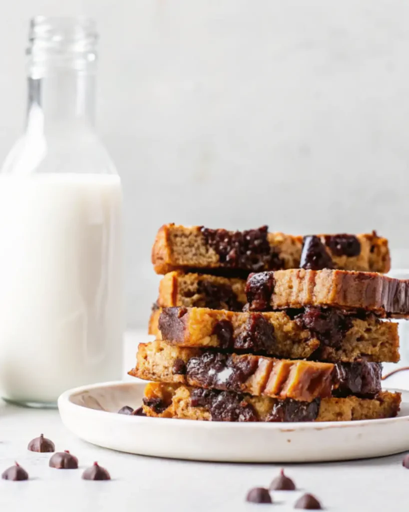 Stacked slices of chocolate-studded banana bread on a white plate next to a milk bottle.