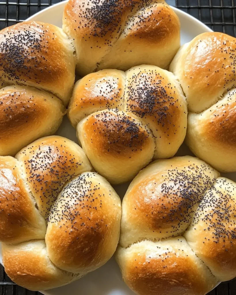 Freshly baked Kaiser rolls topped with poppy seeds on a tray.