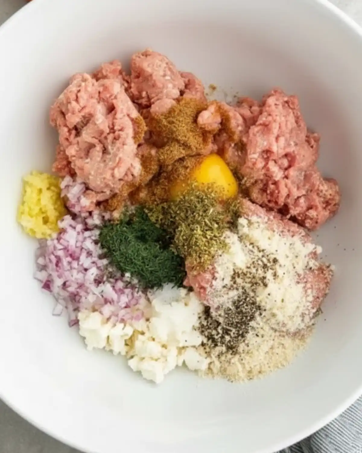 Greek Turkey Meatballs Ingredients for Greek turkey meatballs — ground turkey, feta, red onion, herbs, and spices in a white bowl.